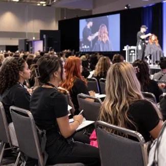 beauty students in an audience watching a hair demonstration on stage