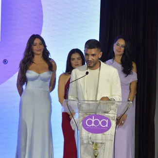 Three women stand behind a man who is accepting an award onstage
