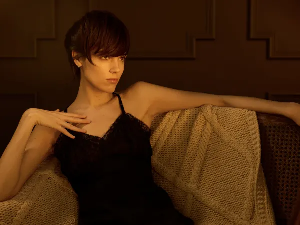 A woman with short brown hair, seated, in a black slip dress