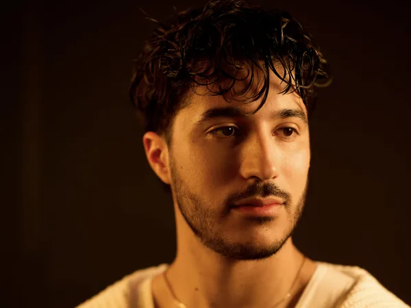 A man with curly dark hair and a white sweater