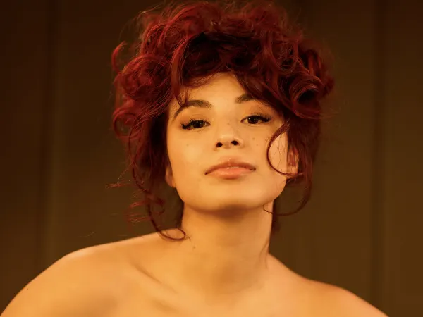A model with red hair in a curly chignon, wearing a black bustierre