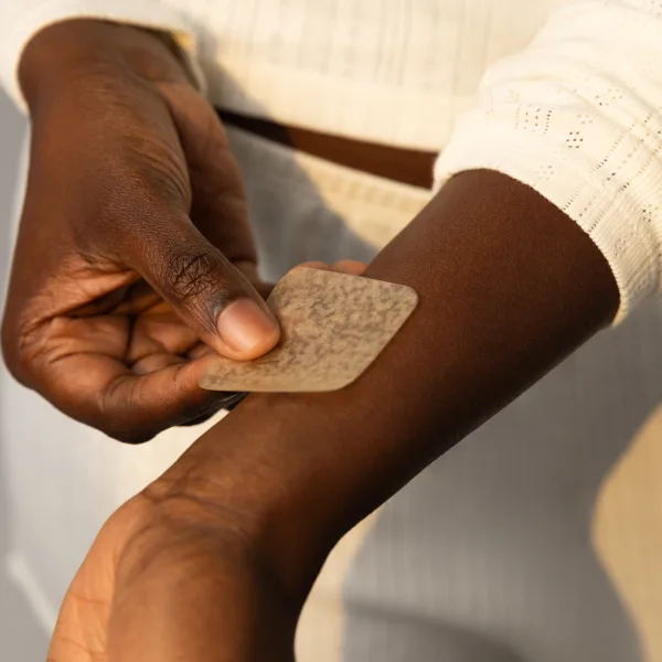 An arm extends while a hand applies a patch to a wrist.