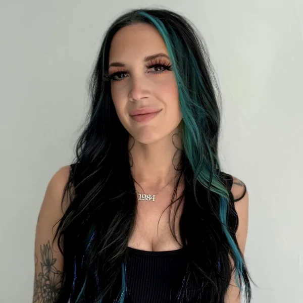 A young woman with long black and green hair, in a black crop top. 