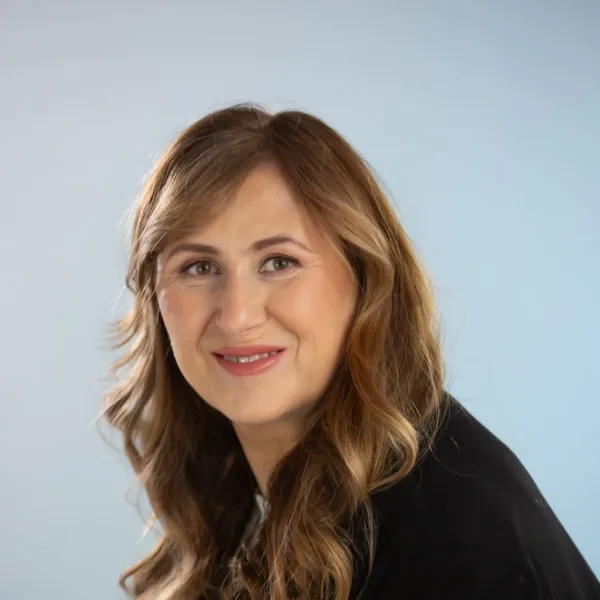 A woman with long blonde hair wears a black blazer.