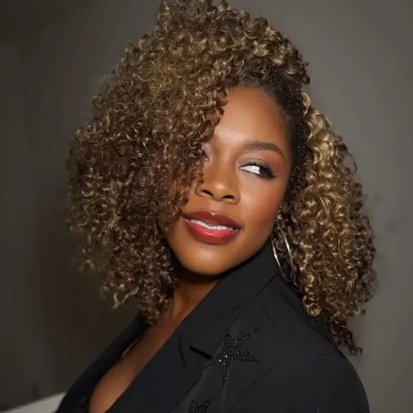 A woman in black, with tight, carmel curls,  looks over her shoulder.