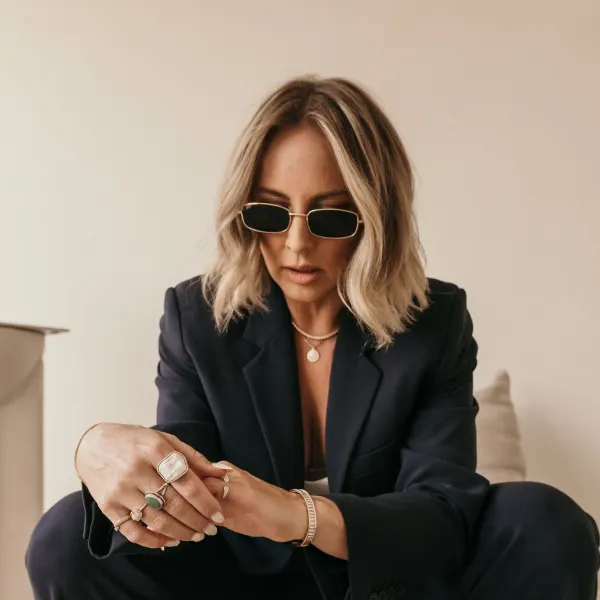 A woman with a short blonde haircut, wearing a suit, sitting, and wearing sunglasses.