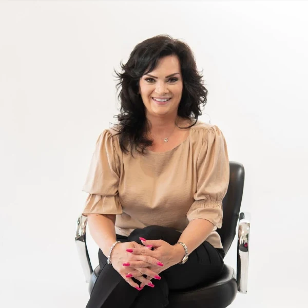 A woman with black hair sits in a salon chair, with crossed legs.