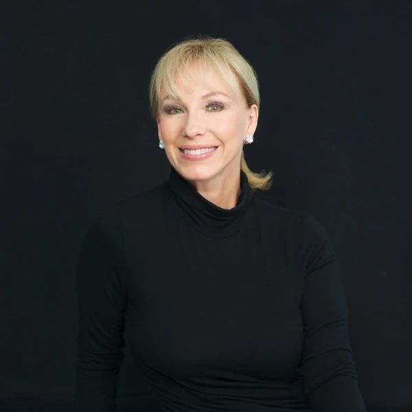 A blonde woman with a ponytail, wearing a black turtleneck and jeans, sitting.