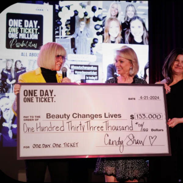 Two happy women, one wearing yellow blazer, are smiling and holding an oversized check.