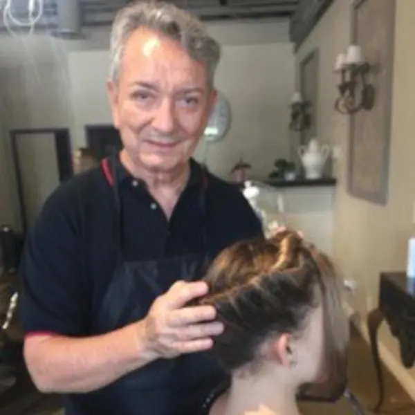 An older male hairstylist behind his client