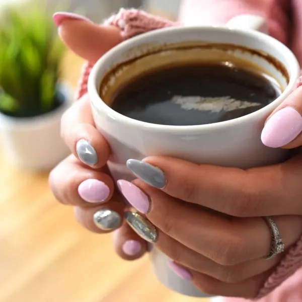 a pair of hands with pink-polished nails holding a cup of black coffee