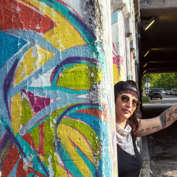 A woman holding a gay pride flag in front of a colorful mural.