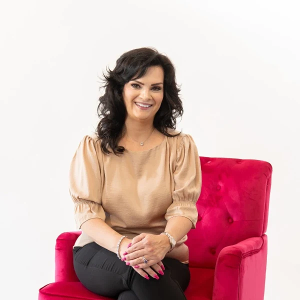 A woman seated, cross-legged, in a pink chair.