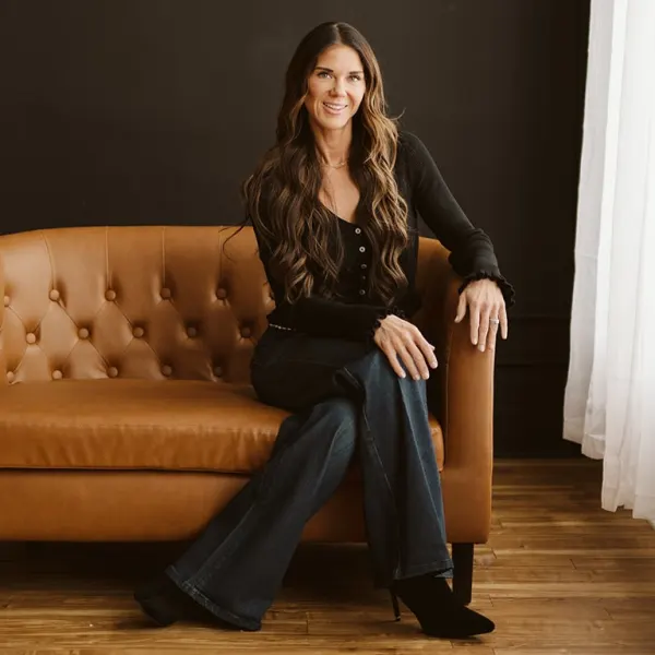Kati Whitledge sits on a brown couch with daylight illuminating her face