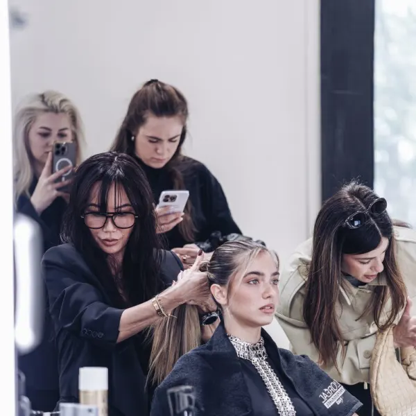 A stylist pulls a model's hair into a ponytail as influencers snap pictures with their iphones