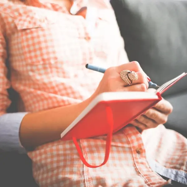 The torso of a woman, writing in a book.