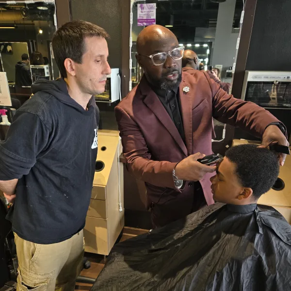 A barbering instructor works on a client while a student observes.
