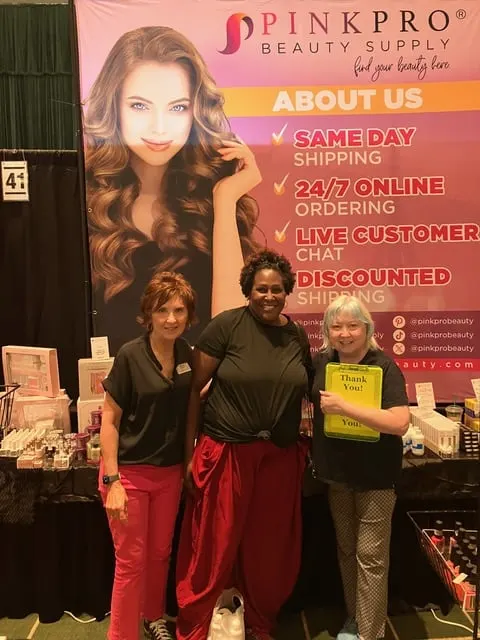 Three women stand in front of a banner advertising nail products