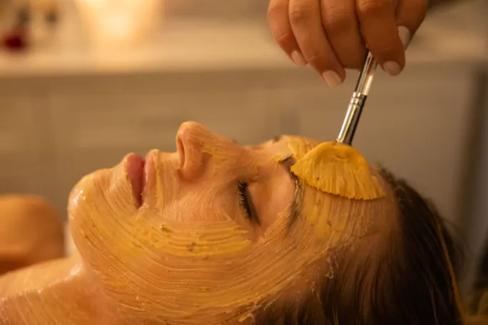 An esthetician paints a mask on a client's face during a facial