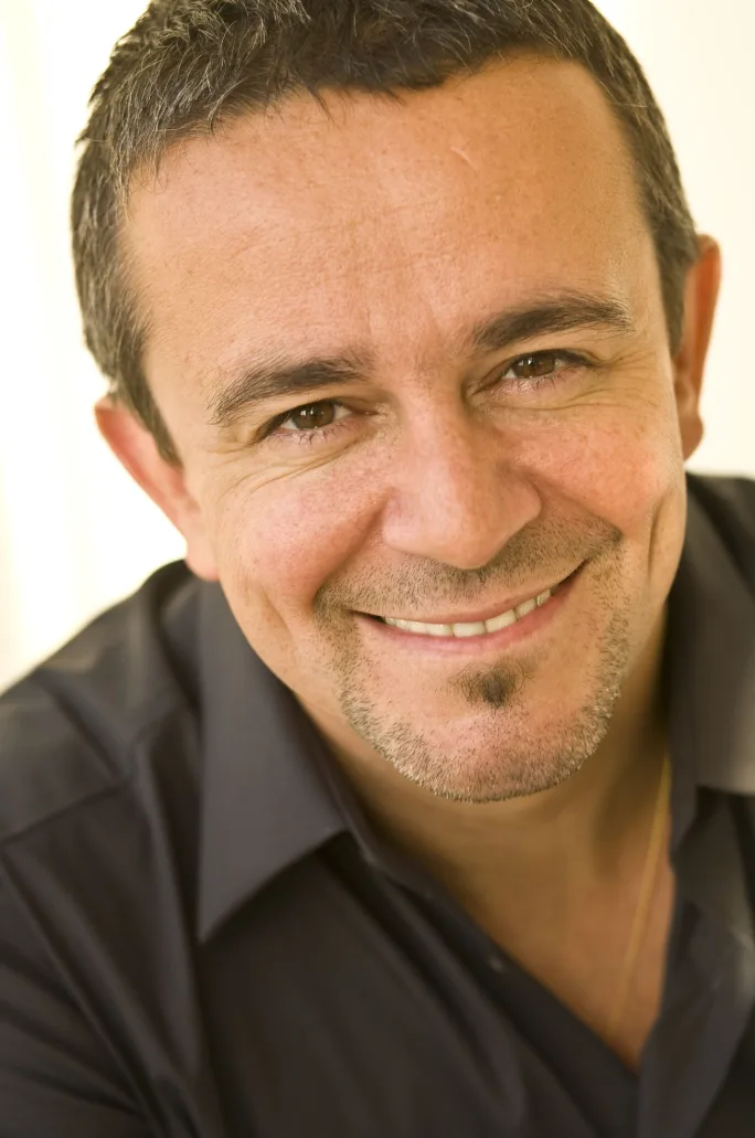 A man with a v-neck brown shirt smiles.