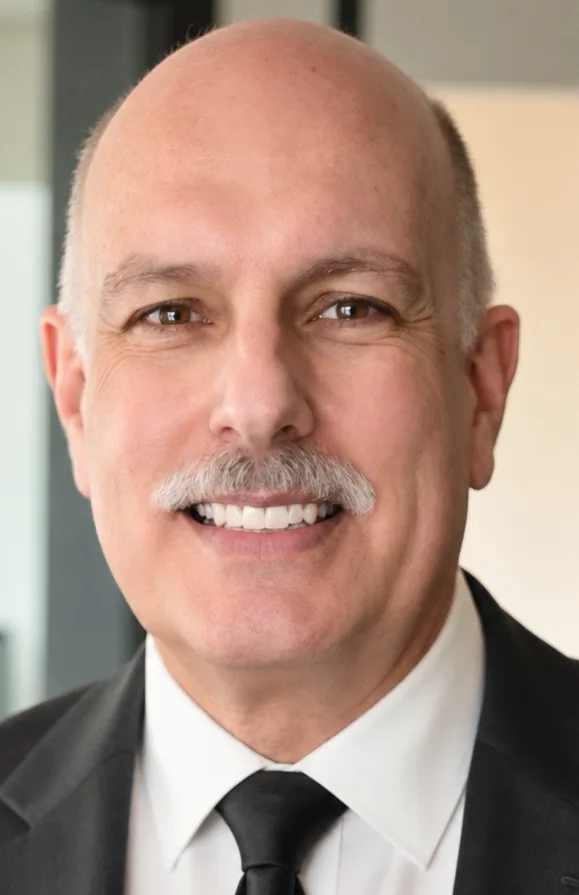 An older man with a bald head, wearing a black suit.