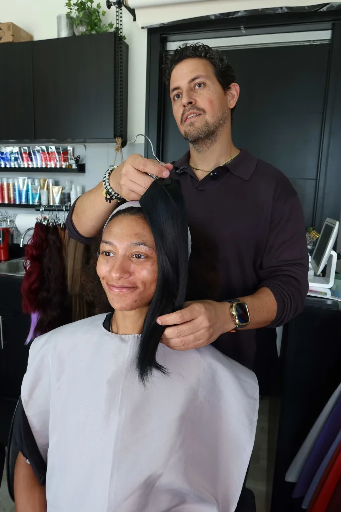A man holds a weft of hair next to a woman's face