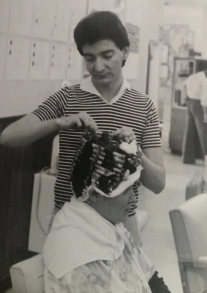 A male hairdresser puts curlers in a woman's hair. 