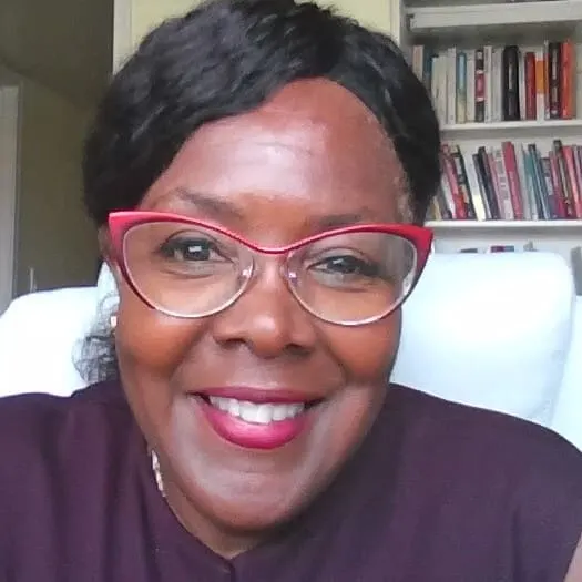 A woman with black hair and red glasses smiles at the camera.