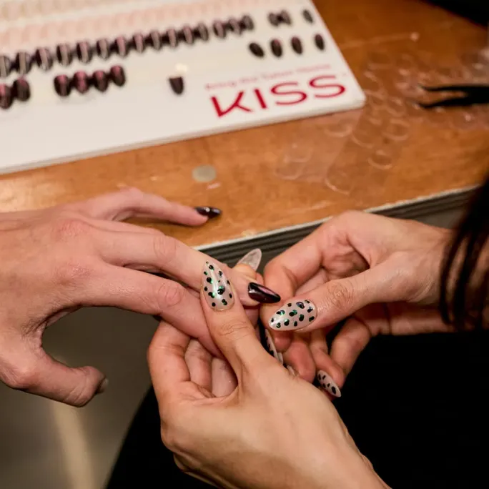 We see a manicurist holding a client's hand and applying false nails. 