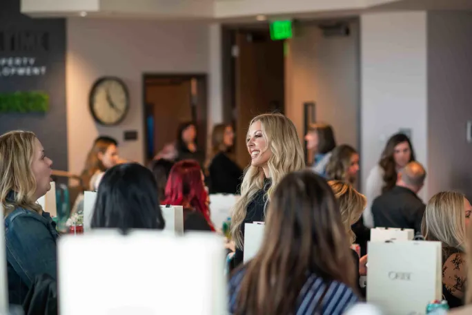 A blonde woman talks to another woman at a trade event.
