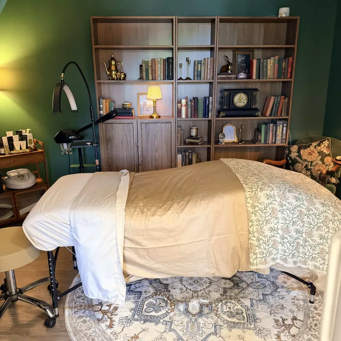 Inside a salon suite, we see a large bookcase, a massage table, a green wall and low lighting.