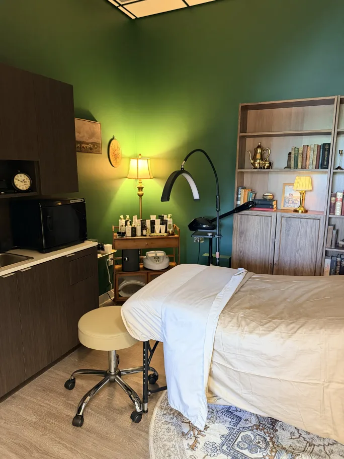 Inside a salon suite, we see the end of a massage table, low lighting, green walls.
