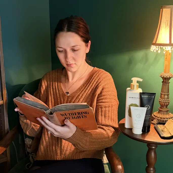 A young woman sits in a wooden chair and reads 