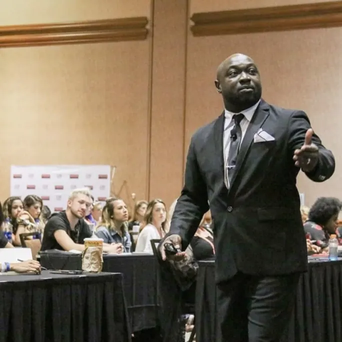 A Black man in a suit, teaches in front of a class