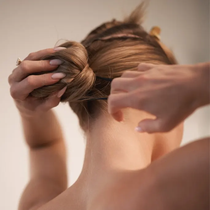 as seen from behind a woman puts her hair into a bun