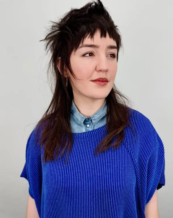 A woman in blue with a shag hair cut, looking to the side