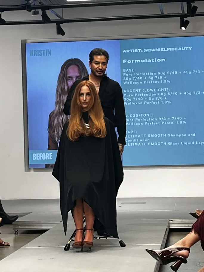 A hairdresser in black stands behind his model onstage