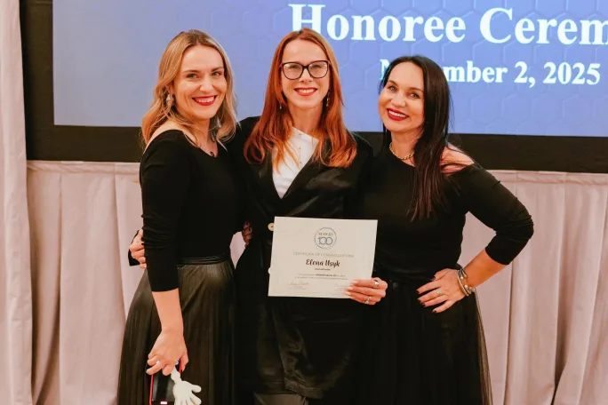 Three women stand onstage together and smile for the camera.