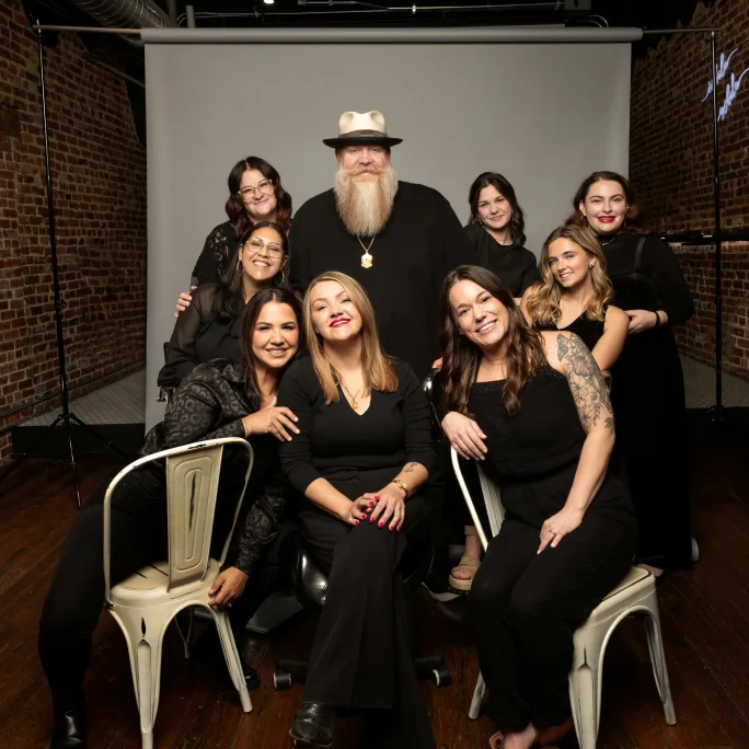 The team from All Things New pose in all black attire on a photo set.