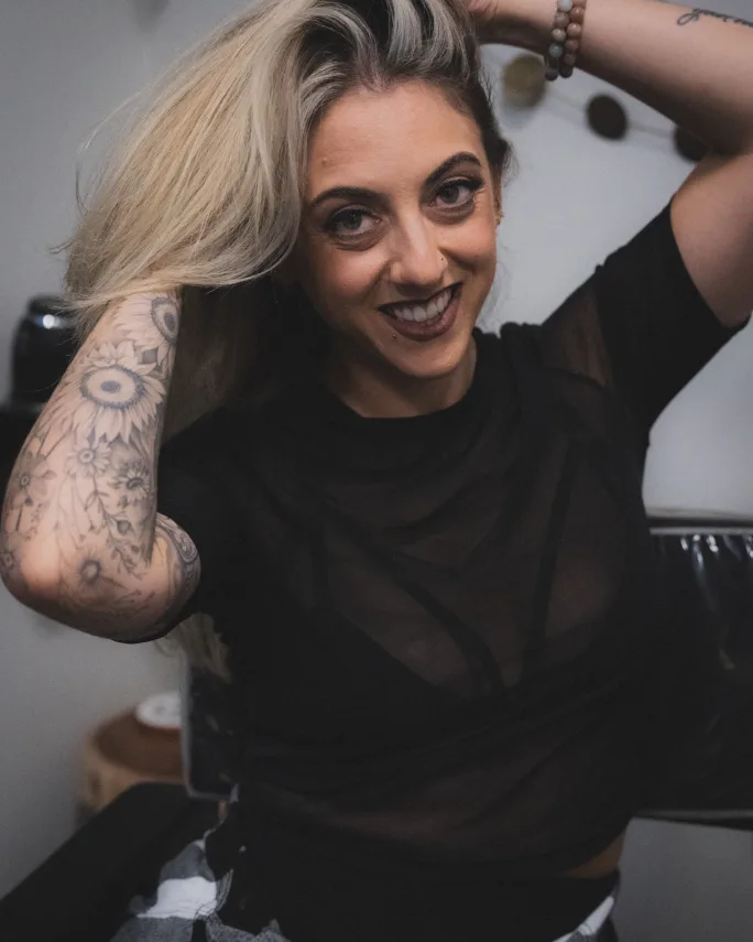 A woman with long hair, her hands in her hair, sitting and smiling.