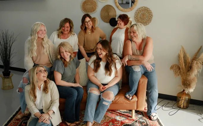Looking at one another and sharing a laugh, a group of people pose on a tan couch.