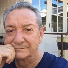 An elderly man with his hand to his face.
