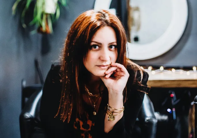A redheaded woman with her hand on her cheek.
