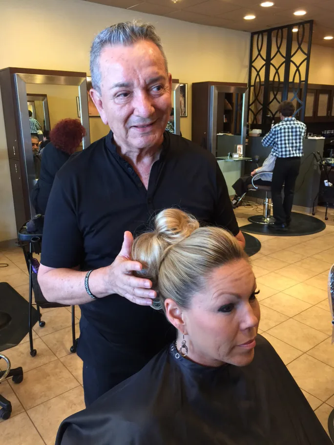 A male stylist stands behind his client and perfects her updo.
