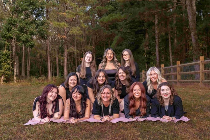 A group of stylist in a pyramid formation on top of pink towels in a forest setting.