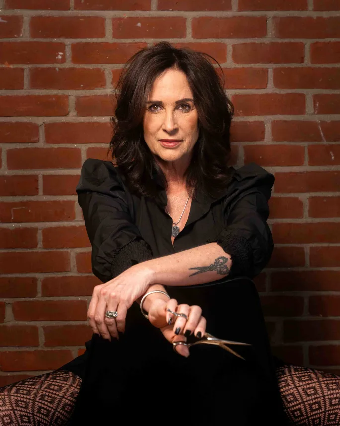With a brick wall as the background, Dawn Blom is seated with her shears in hand.