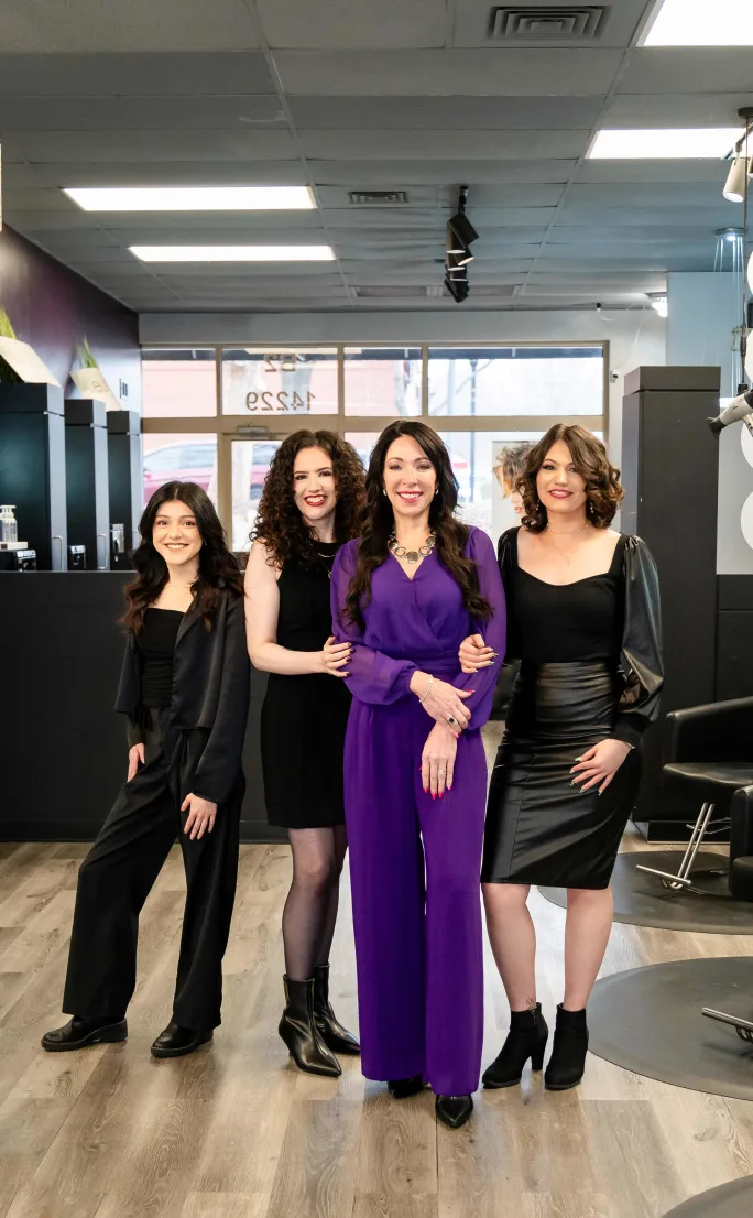 One woman dressed in purple is flanked by her stylists dressed in black in their salon.