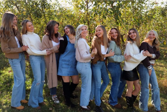A group of stylists pose arm in arm while looking at one another in front of a group of trees.