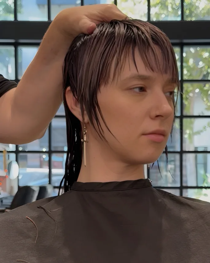Stylist shaping the side section near the ear, leaving a longer point in front of the ear.