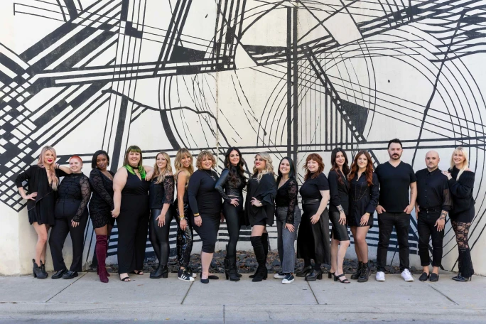 Dressed in black, the team from Harlow Beauty pose in front of a black and white mural on a building.